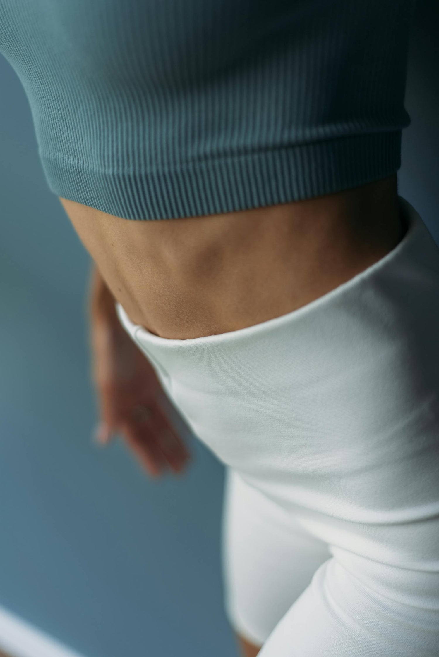 Femme au ventre plat portant un haut de sport gris et un short blanc ajusté, illustrant une silhouette tonique et sportive, parfaite pour les activités fitness et bien-être